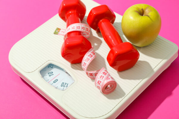 Dumbells, fruit, and a measuring tape on top of a weigh scale